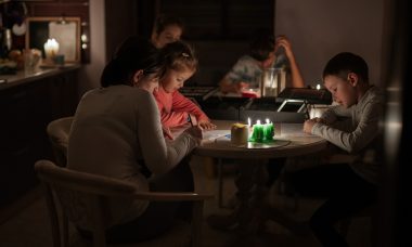 Voksne og børn sidder ved bord med stearinlys
